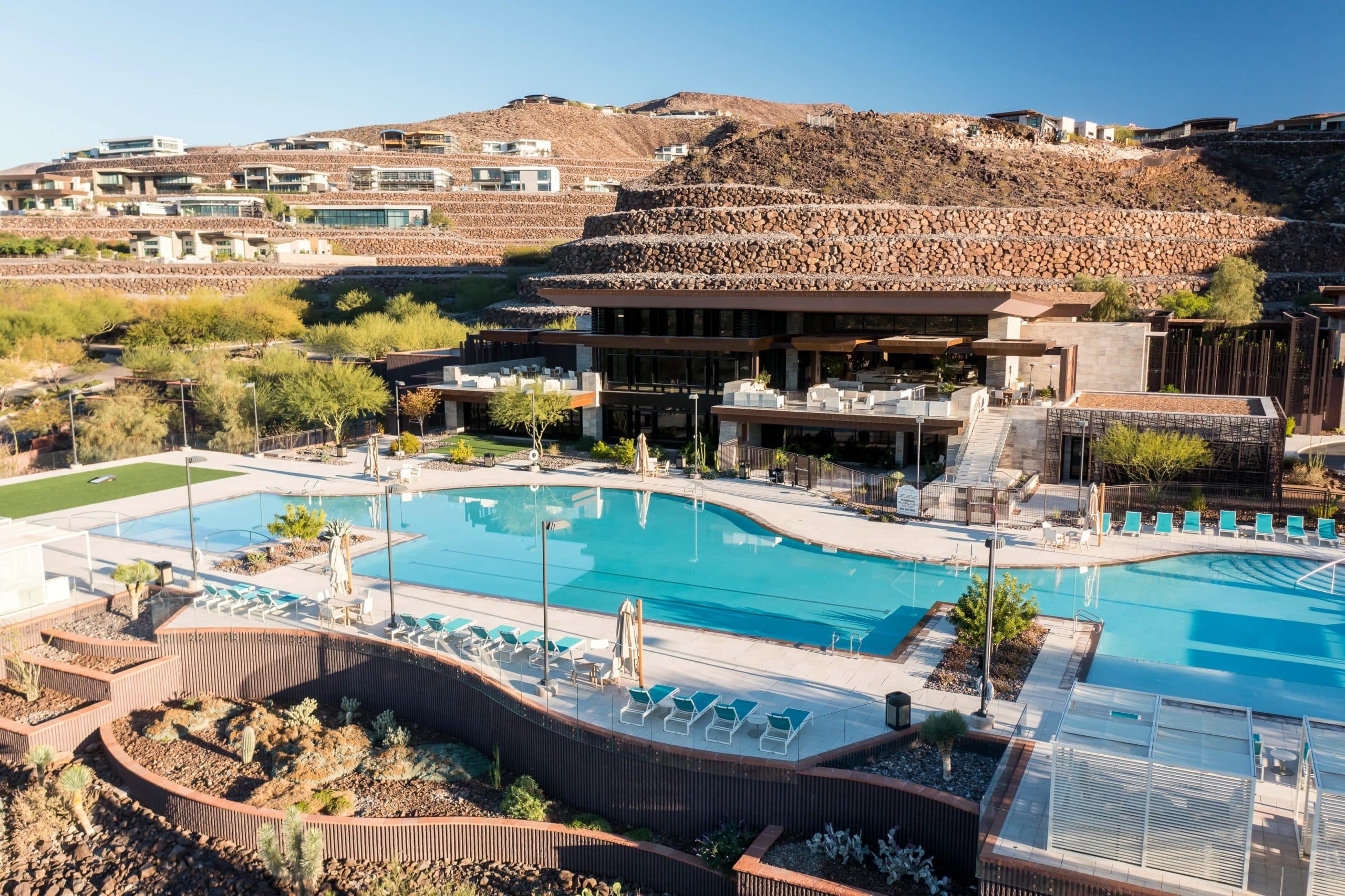 Modern clubhouse and pool area set against desert hills with lounge seating and landscaped grounds.