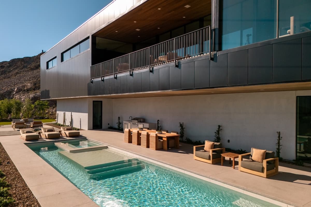 Modern outdoor pool and patio with lounge seating overlooking desert mountains at dusk.
