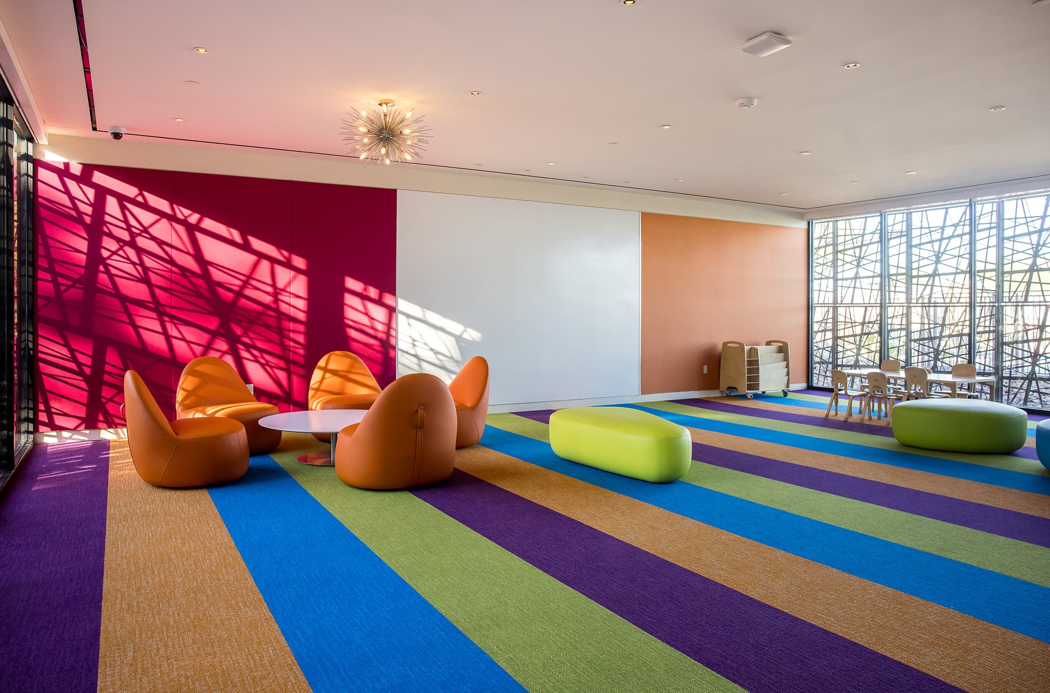 A vibrant children’s playroom with colorful flooring, modern seating, and open space designed for kids to relax, play, and gather.