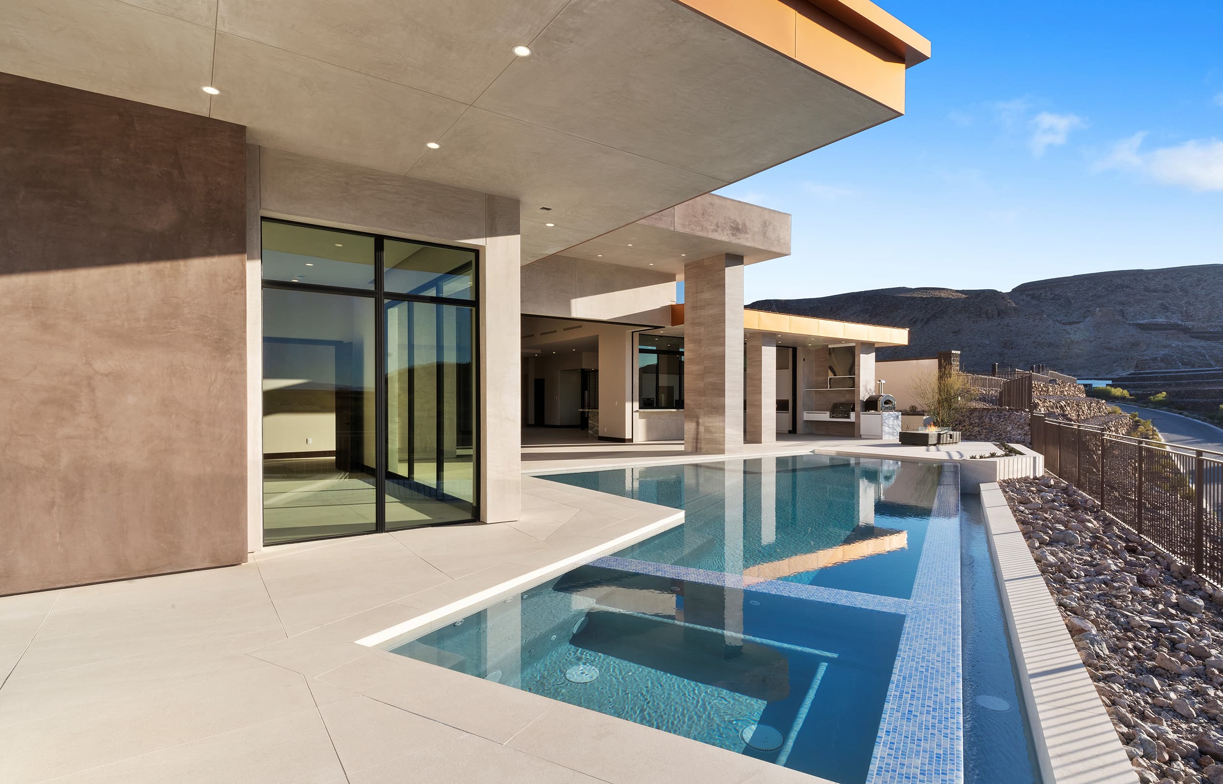 Modern desert contemporary home with a sleek outdoor pool, expansive covered patio, and floor-to-ceiling glass walls overlooking the surrounding mountain landscape.