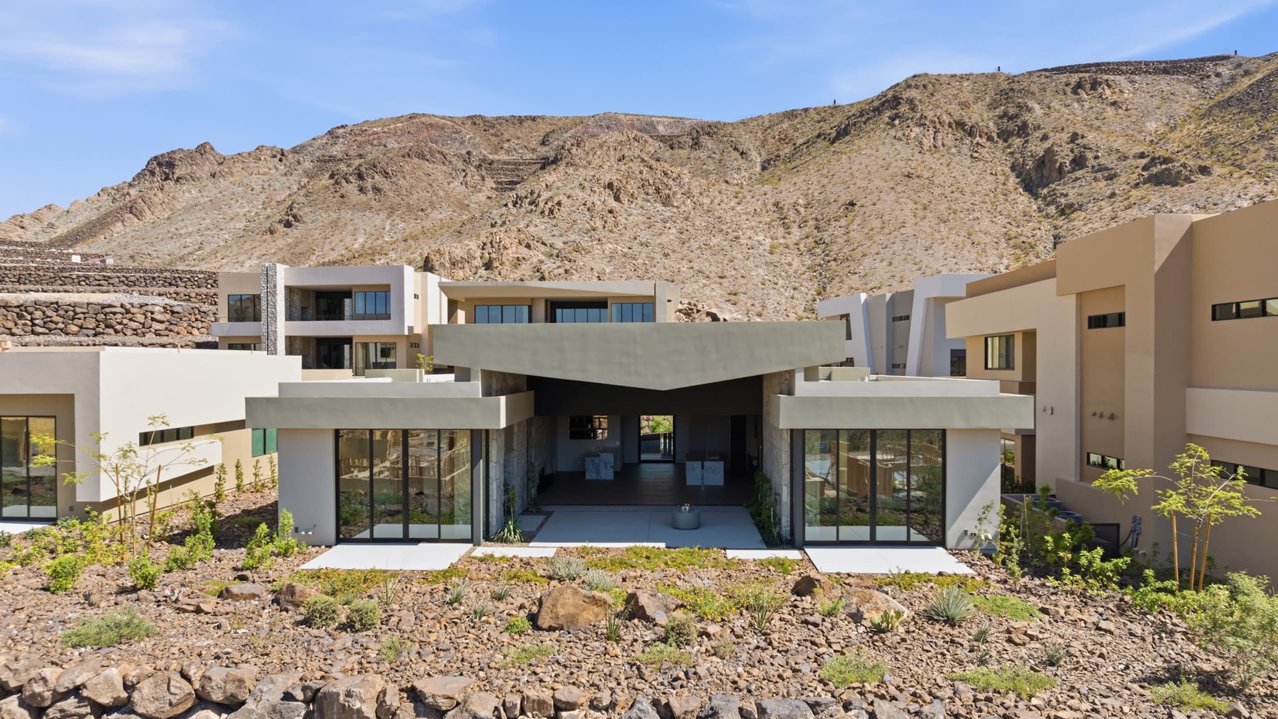 Contemporary luxury home exterior with clean modern lines, expansive glass walls, desert landscaping, and mountain surroundings in an upscale hillside residential community.