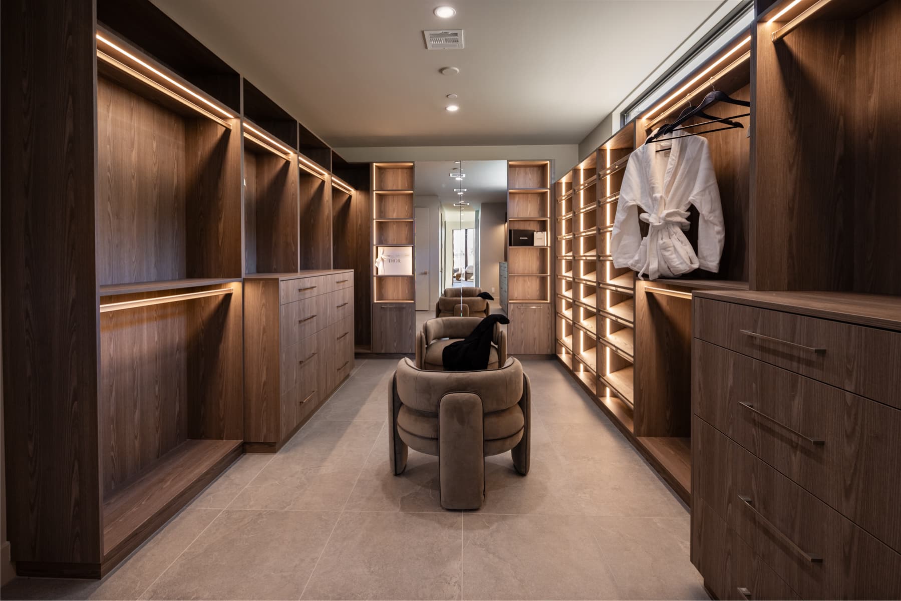 Custom walk-in closet with illuminated wood cabinetry, open shelving, integrated drawers, and boutique-inspired dressing area