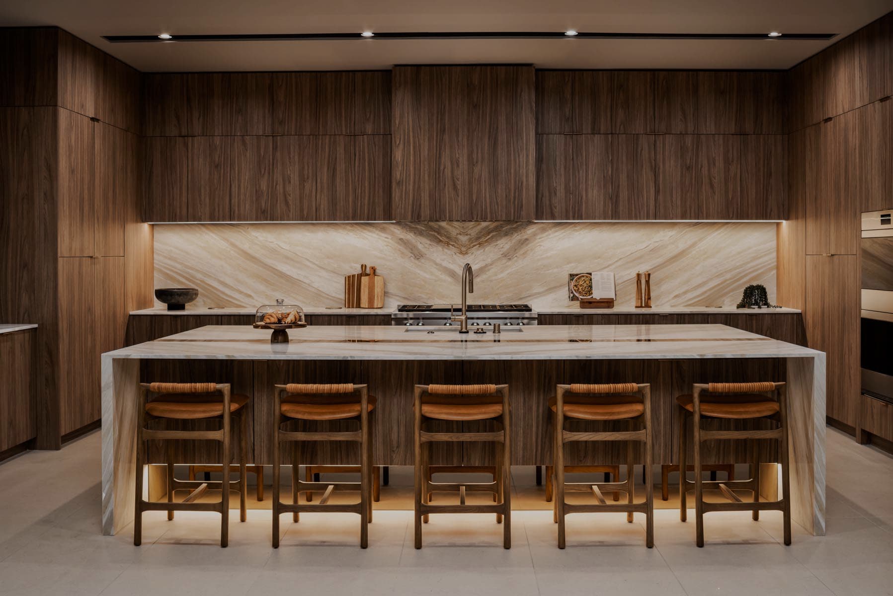 Modern luxury kitchen with dark wood cabinetry, marble waterfall island, bar seating, and high-end appliances.