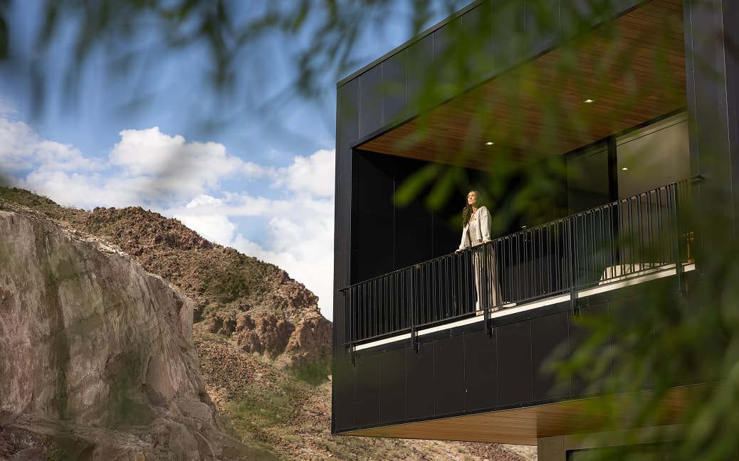 Woman standing on modern luxury home balcony overlooking desert mountains and scenic landscape.