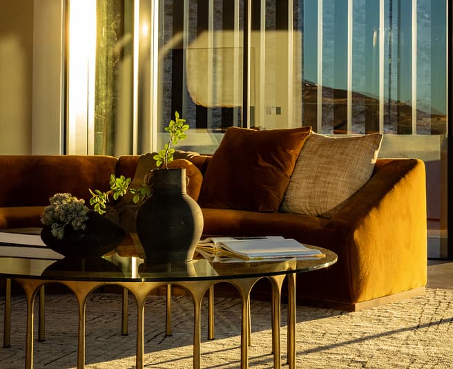 Modern luxury living room with velvet sofa, glass coffee table, and warm natural sunlight through large windows.