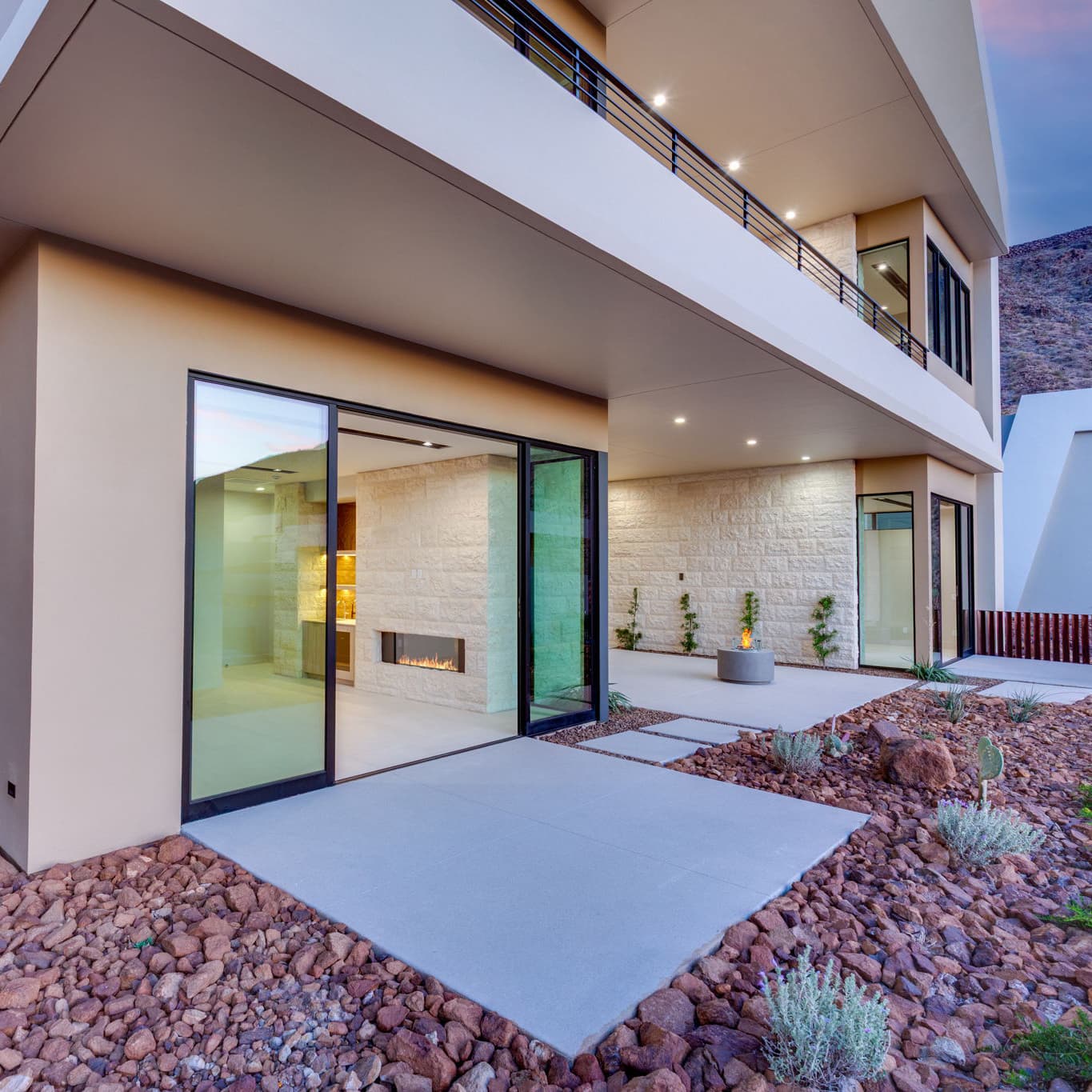 Covered patio with floor-to-ceiling glass doors, linear fireplace, fire feature, and landscaped desert surroundings