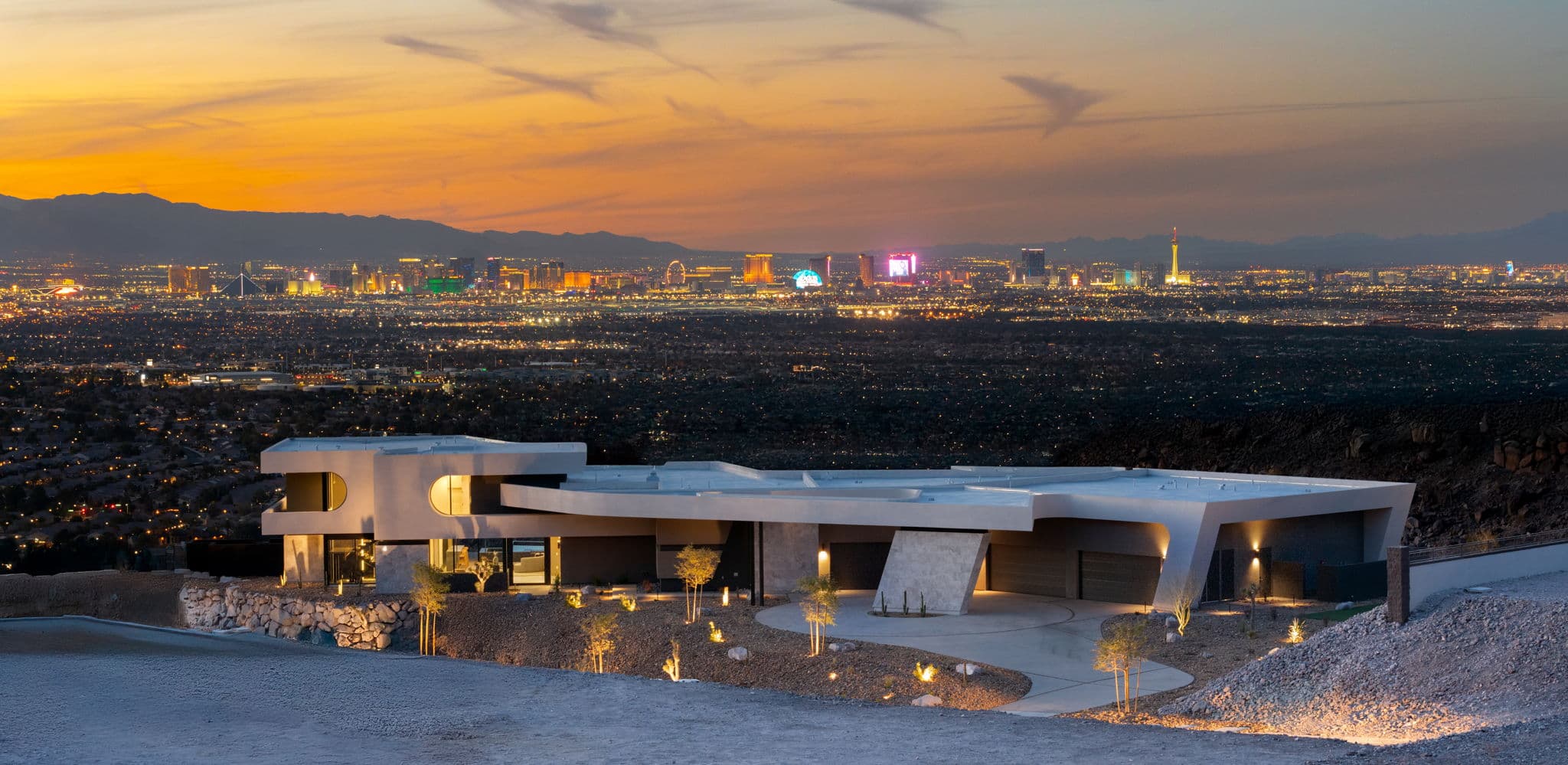 Modern luxury hillside home overlooking the Las Vegas Strip at sunset, featuring contemporary architecture and panoramic city skyline views.