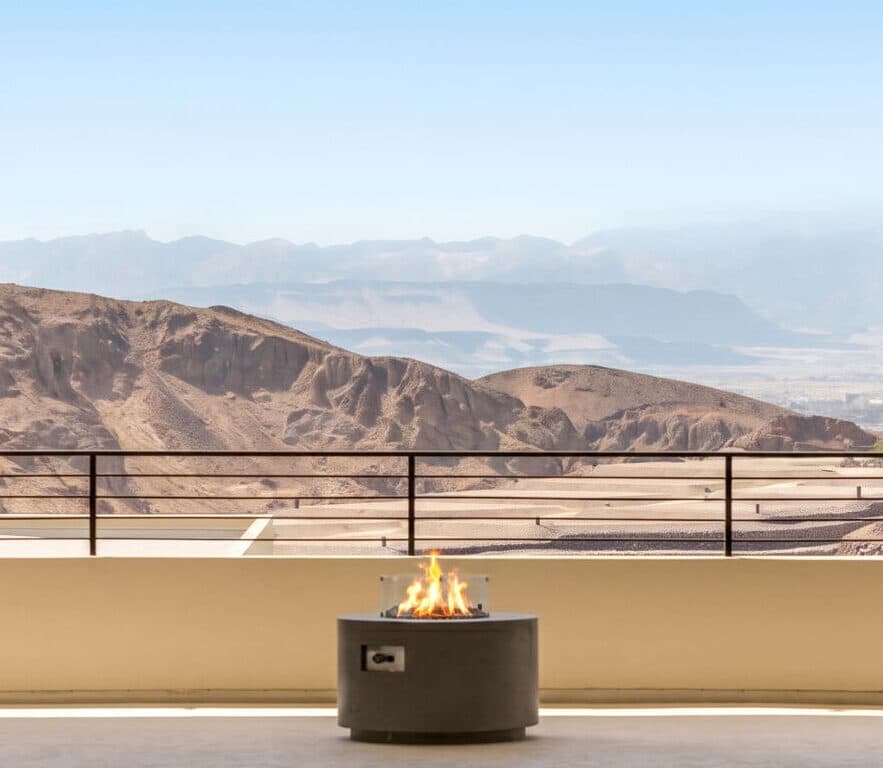 Covered outdoor terrace with modern fire feature and panoramic desert mountain views overlooking terraced homesites and rugged canyon landscape