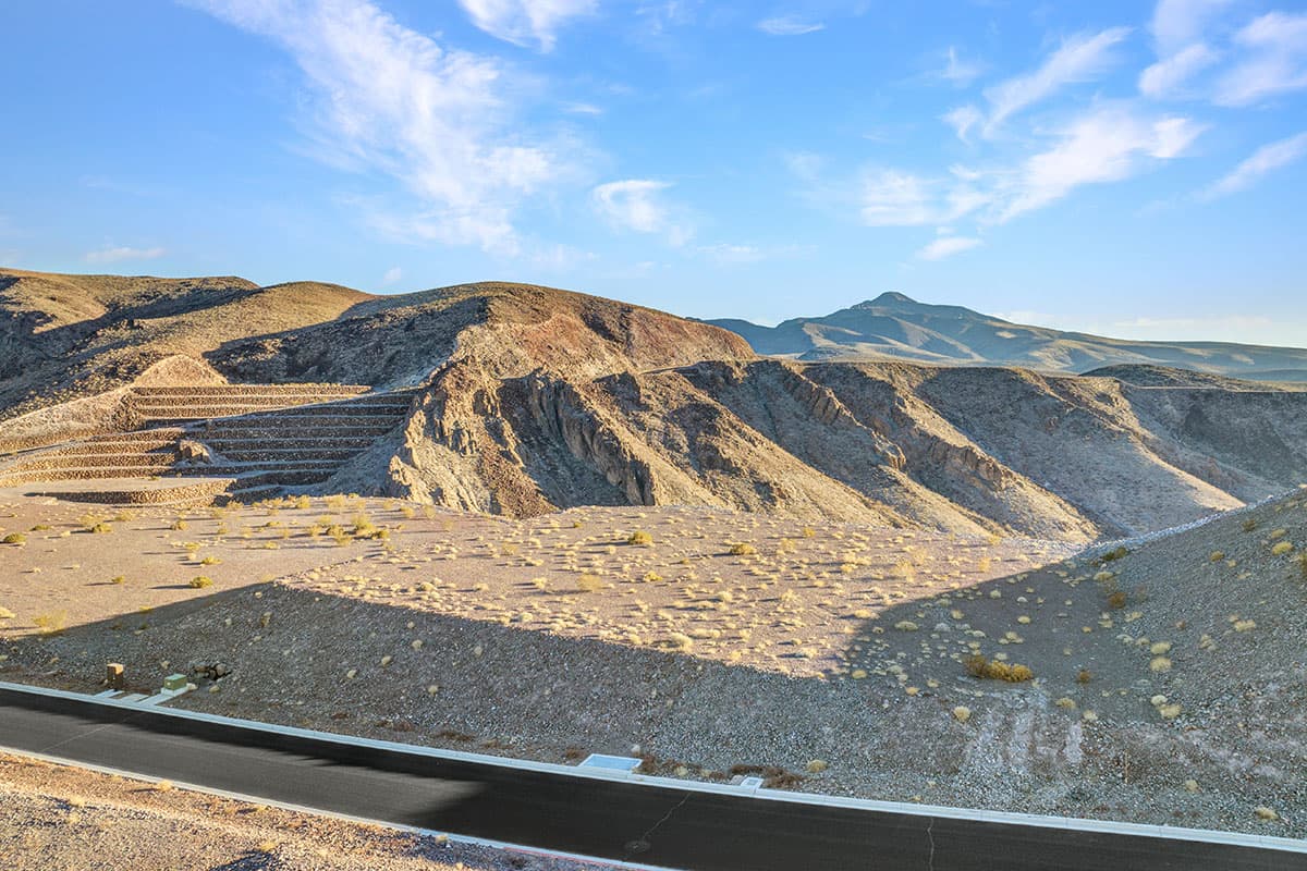 Elevated Ascaya homesite featuring dramatic terraced desert terrain, striking canyon formations, and panoramic mountain vistas beneath expansive blue skies