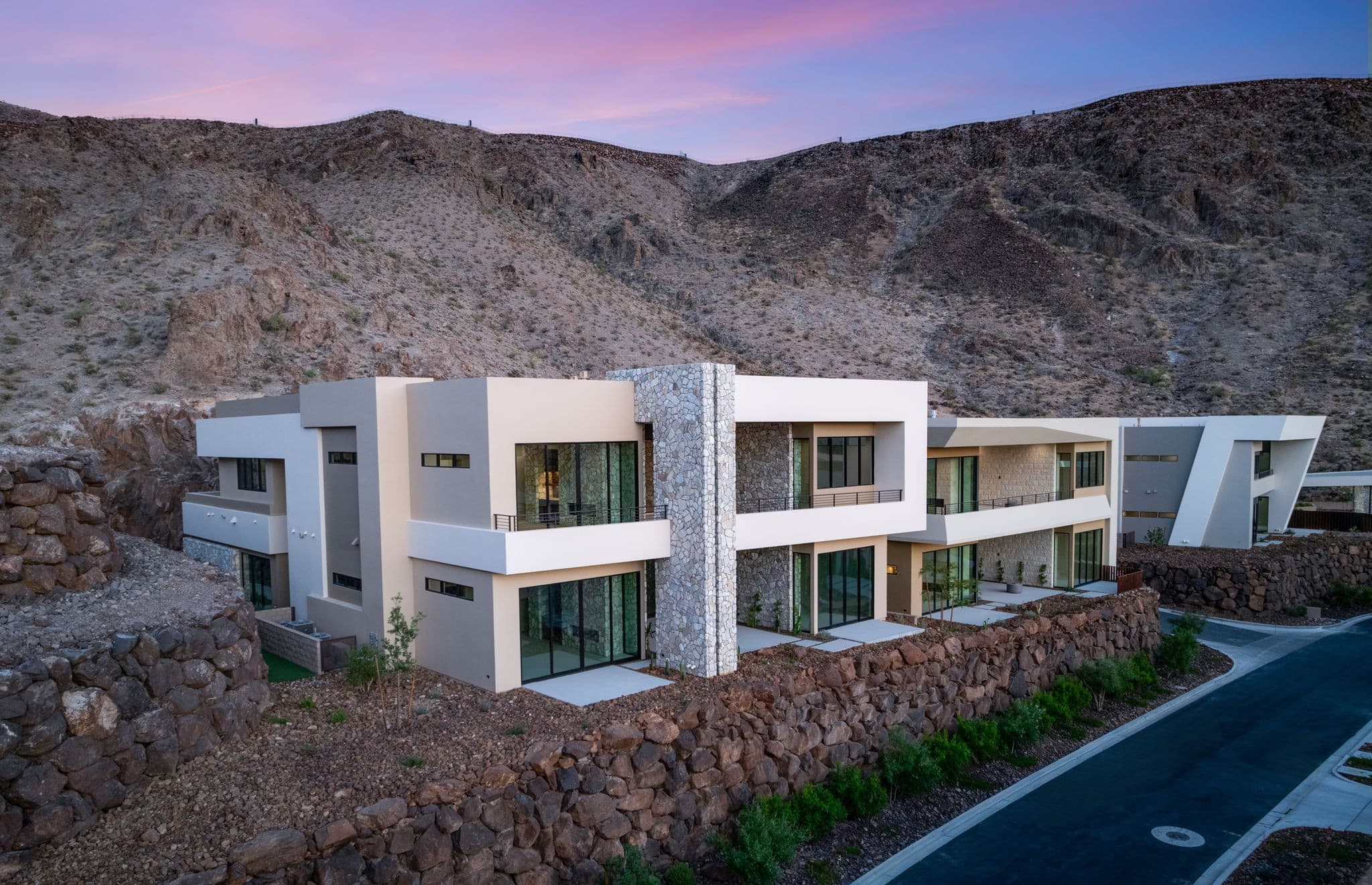 Modern desert hillside home with stone accents, large windows, and a twilight sky backdrop.