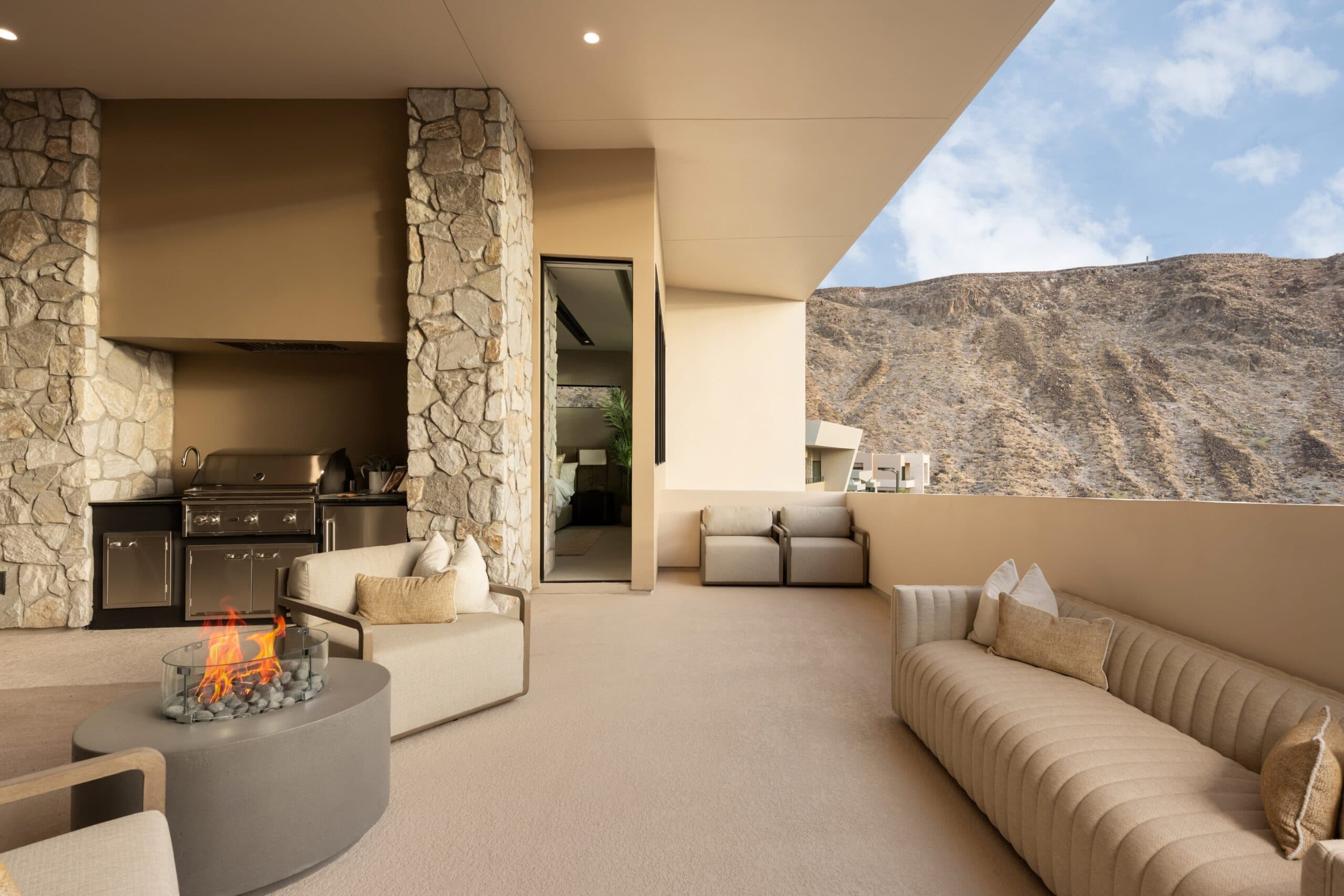 Luxury covered outdoor lounge with a fire pit, built-in grill, stone accents, and panoramic mountain views.