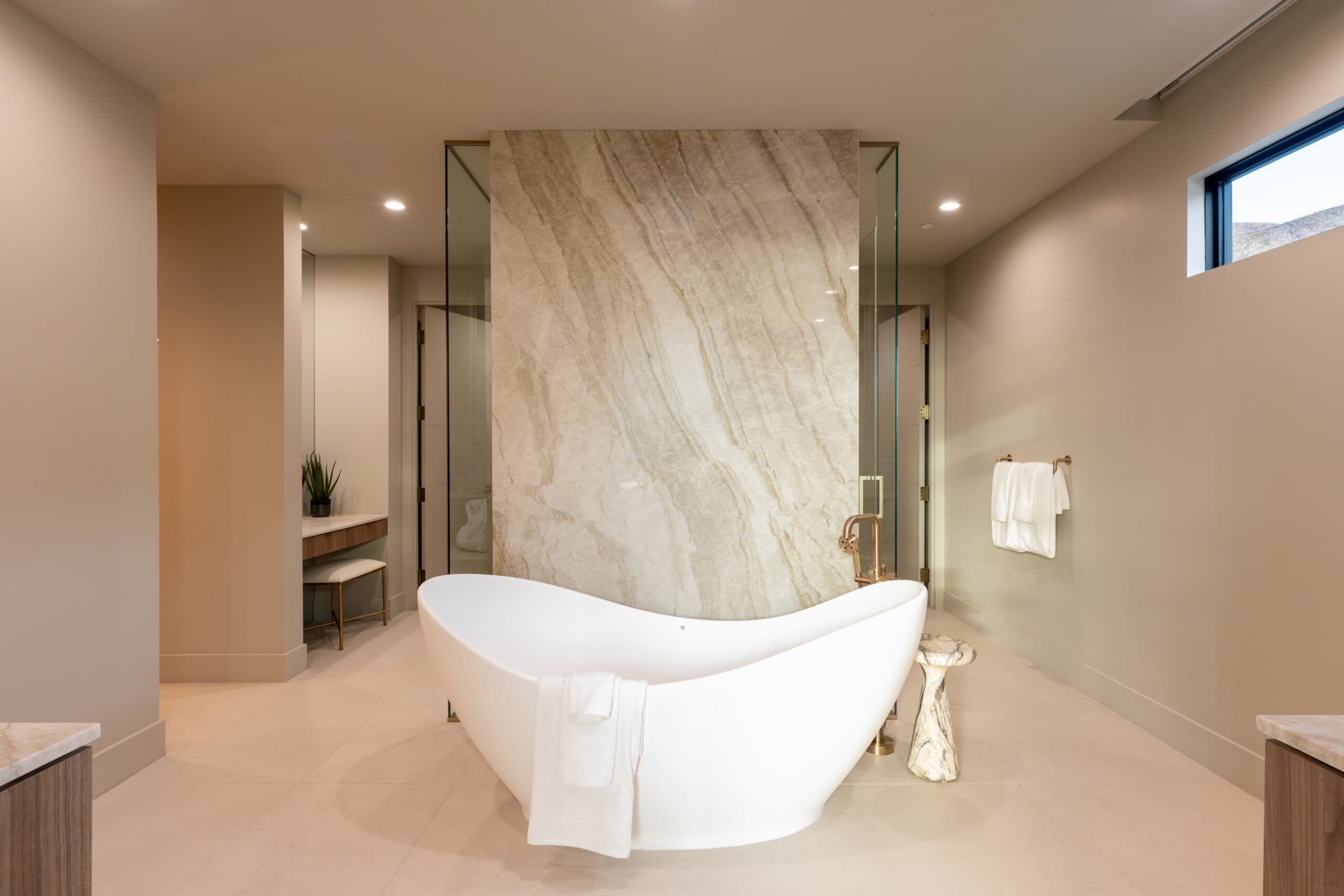 Luxury spa-inspired bathroom with a sculptural freestanding tub, dramatic stone feature wall, and glass-enclosed shower.