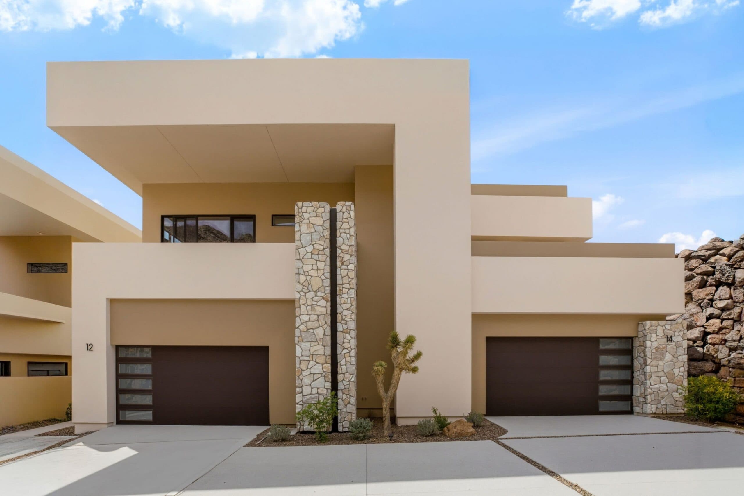 Modern luxury desert home exterior with clean geometric architecture, stone accents, dual garages, and minimalist landscaping.