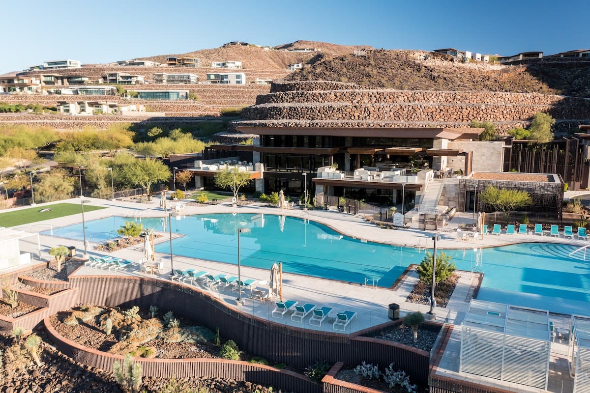 Modern clubhouse and pool area set against desert hills with lounge seating and landscaped grounds.
