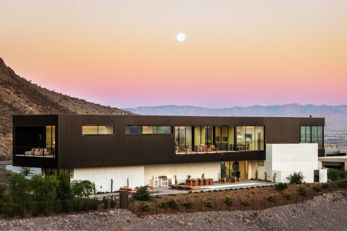 Contemporary desert home with expansive windows set against a pastel sunset sky and mountain backdrop.