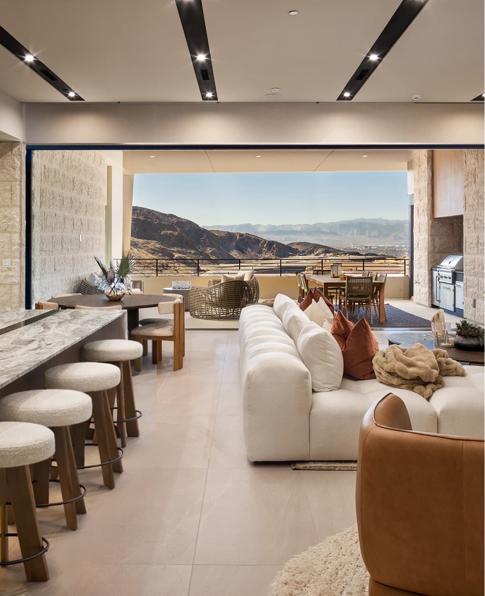 Luxury open-concept kitchen and living room with marble island, modern seating, and expansive indoor-outdoor desert mountain views.