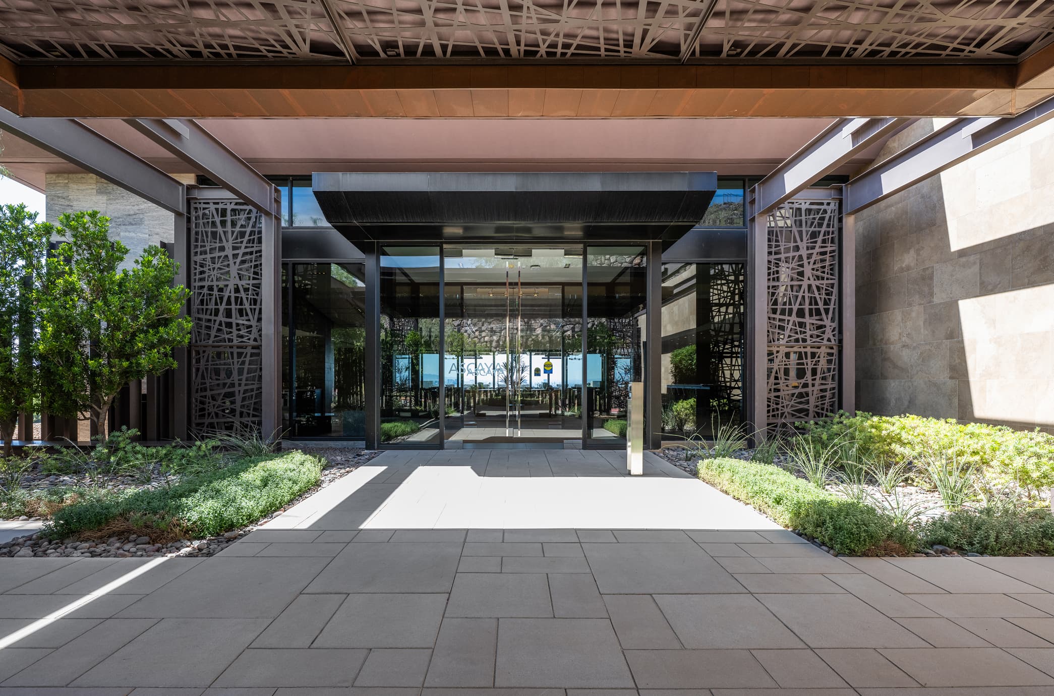 Modern glass-front entrance with metal canopy and landscaped walkway leading to a contemporary building.