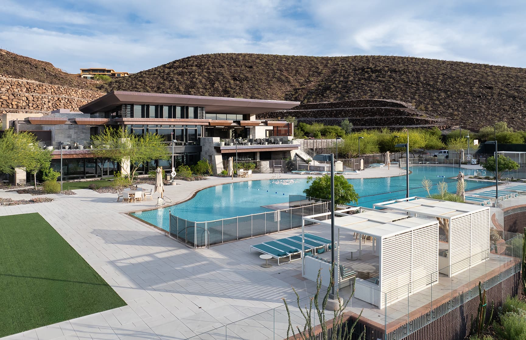 A view of the Ascaya clubhouse and resort-style pool, showcasing the expansive zero-edge pool, private cabanas, lounge seating, and surrounding desert landscape.