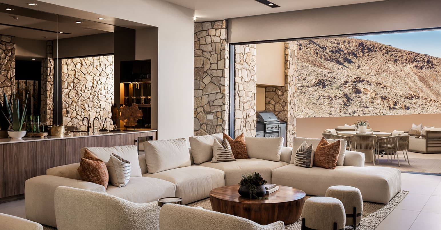 Modern open-concept living room with plush sectional sofa, stone accent walls, indoor-outdoor flow, and luxury desert mountain views.