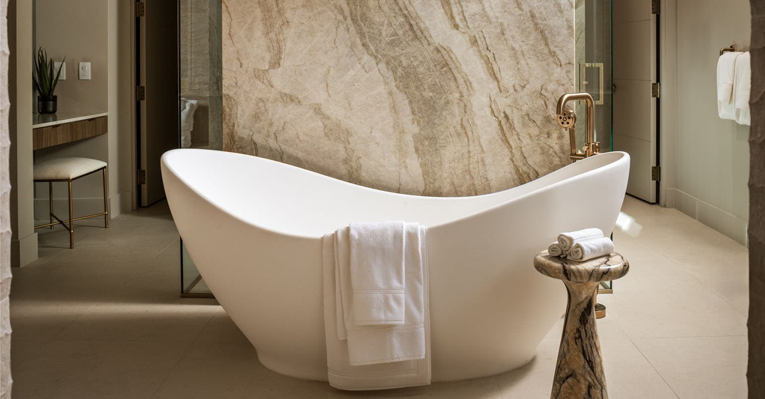 Luxury modern bathroom with freestanding soaking tub, marble feature wall, glass shower, and elegant gold fixtures.