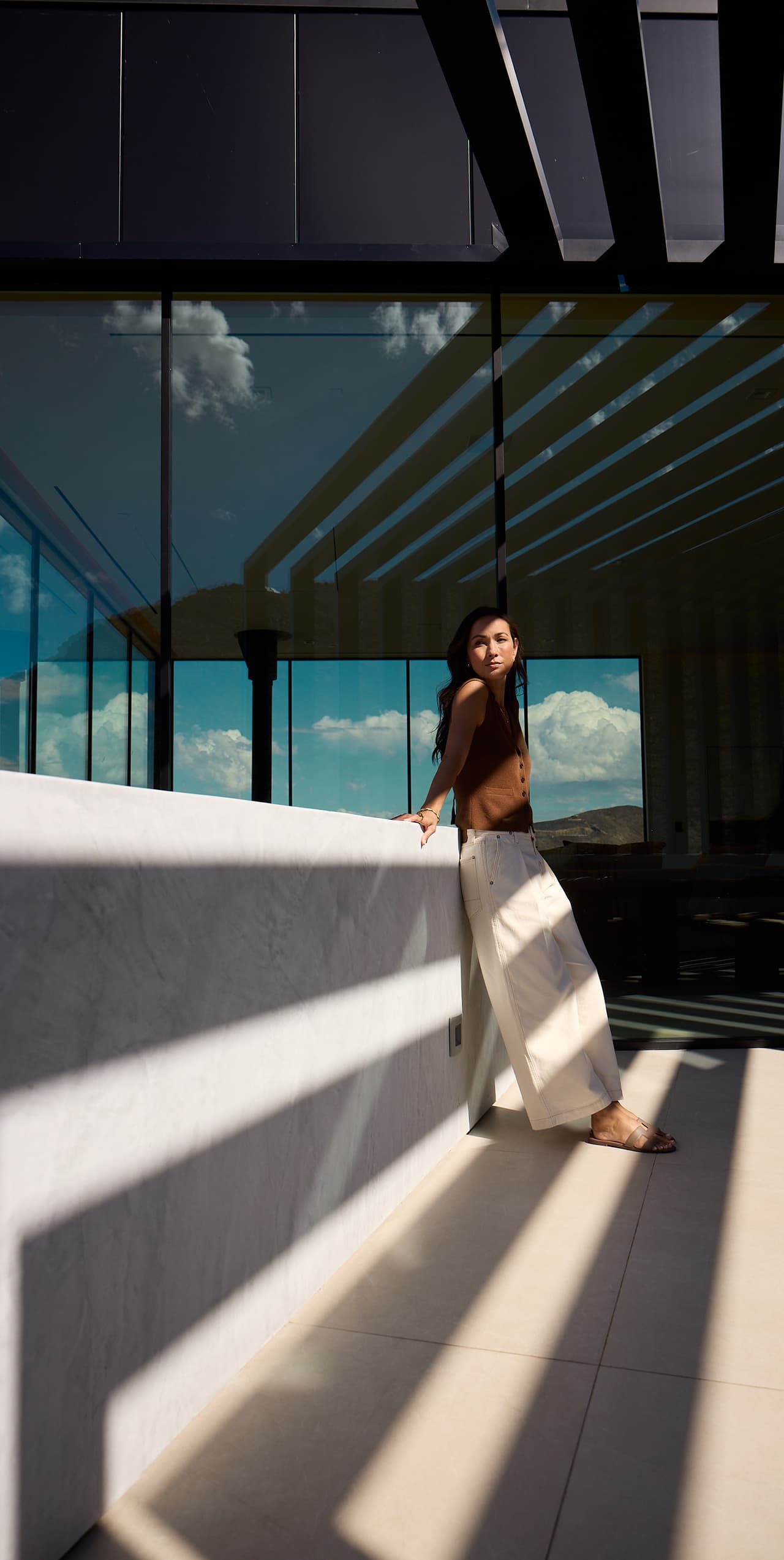 Woman relaxing on modern luxury home balcony with floor-to-ceiling glass and desert views.