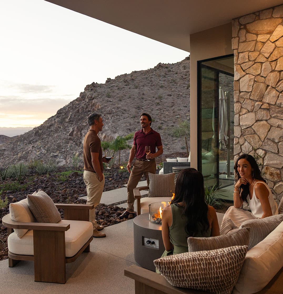 Friends enjoying drinks on a modern desert patio with fire pit and mountain views at sunset.