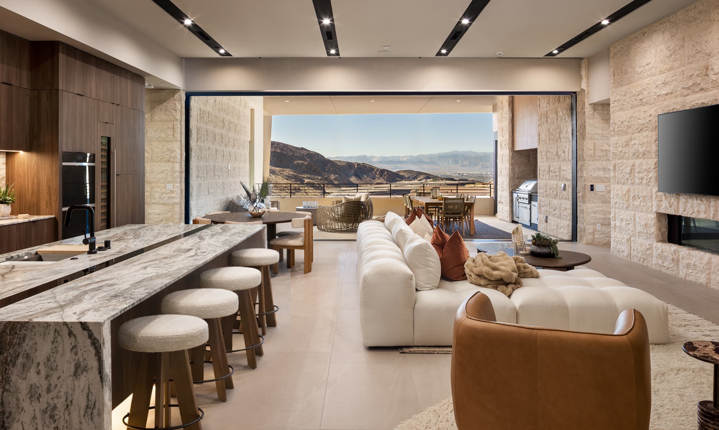 Luxury open-concept kitchen and living room with marble island, modern seating, and expansive indoor-outdoor desert mountain views.
