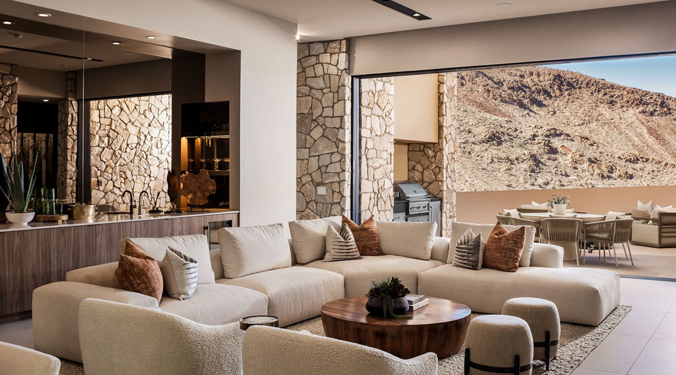 Modern open-concept living room with plush sectional sofa, stone accent walls, indoor-outdoor flow, and luxury desert mountain views.