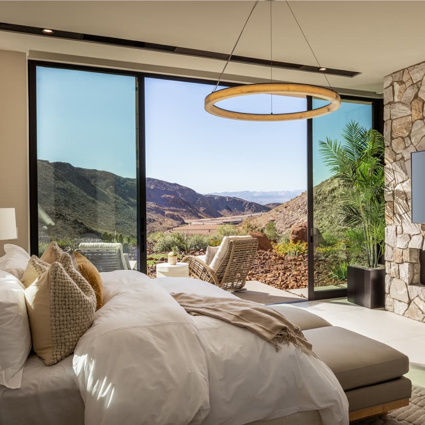 Modern luxury bedroom with stone fireplace, large glass doors, and scenic desert mountain views.