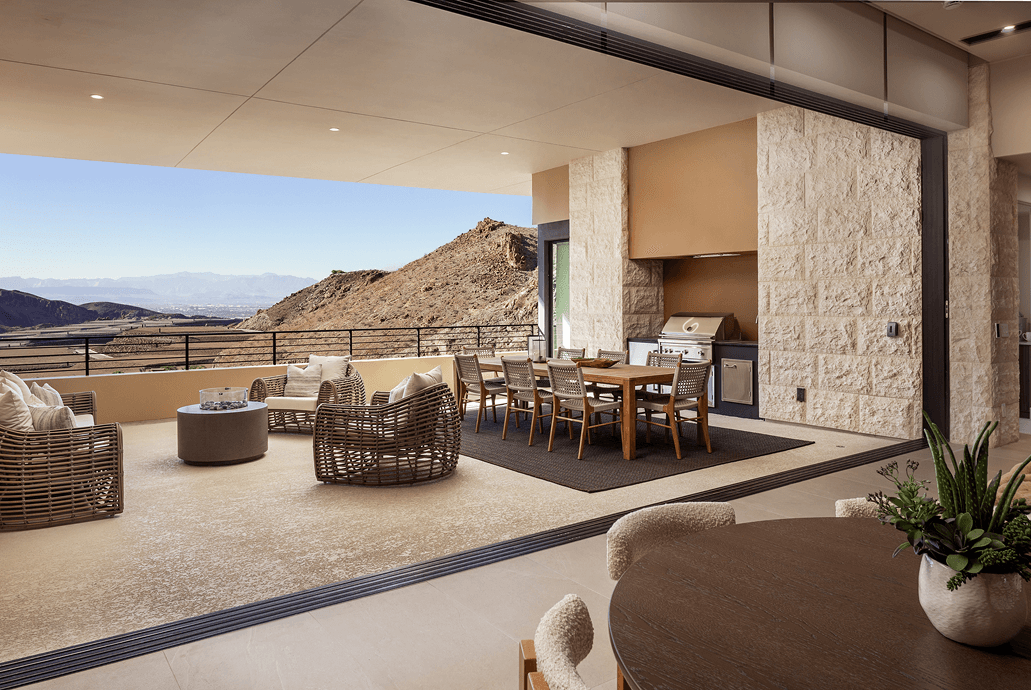 Covered outdoor terrace with lounge seating, dining area, and built-in grill, overlooking rugged desert hills and expansive valley views.