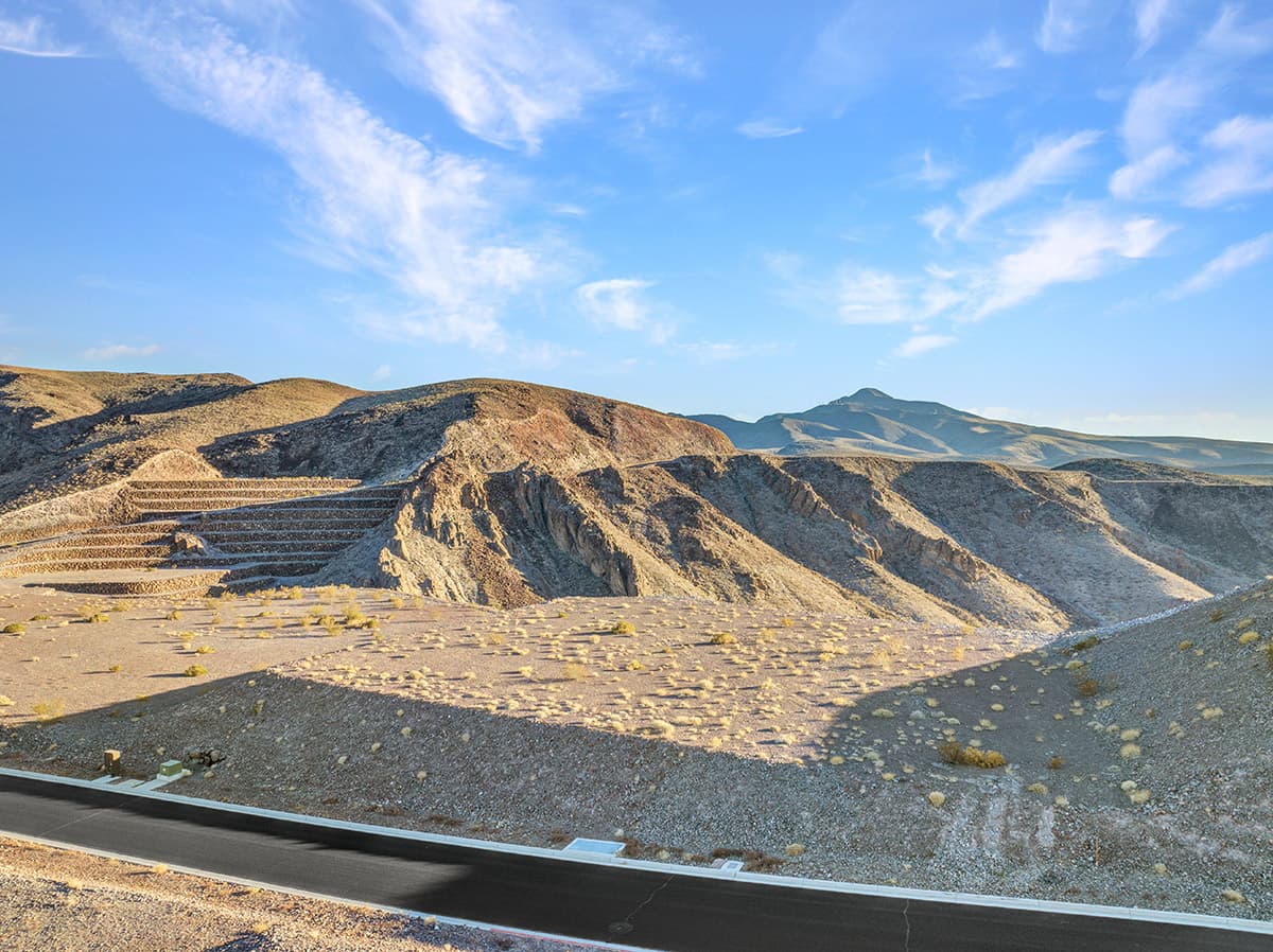 Elevated Ascaya homesite featuring dramatic terraced desert terrain, striking canyon formations, and panoramic mountain vistas beneath expansive blue skies