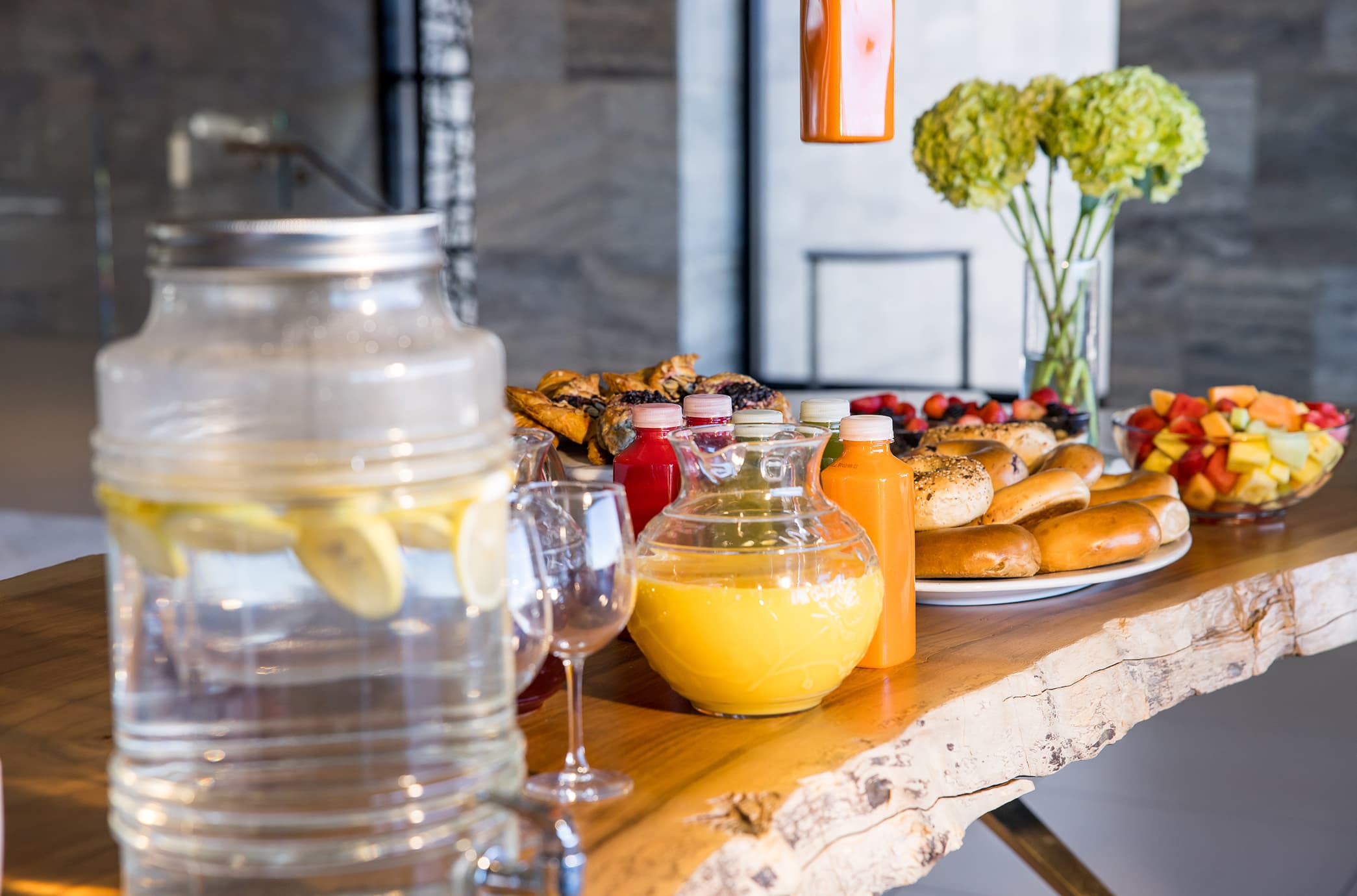 A catering spread in the clubhouse featuring fresh juices, pastries, bagels, fruit, and infused water, elegantly arranged for a social gathering.