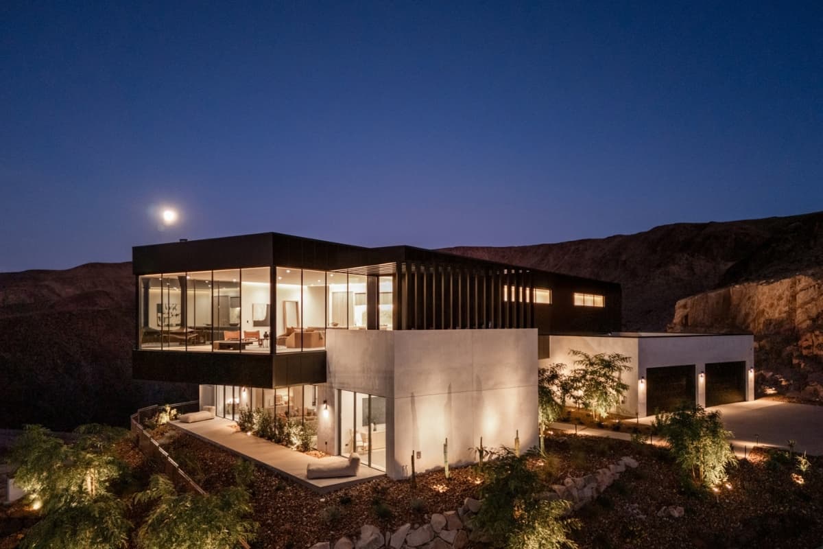 Modern luxury desert home illuminated at night beneath a moonlit sky.