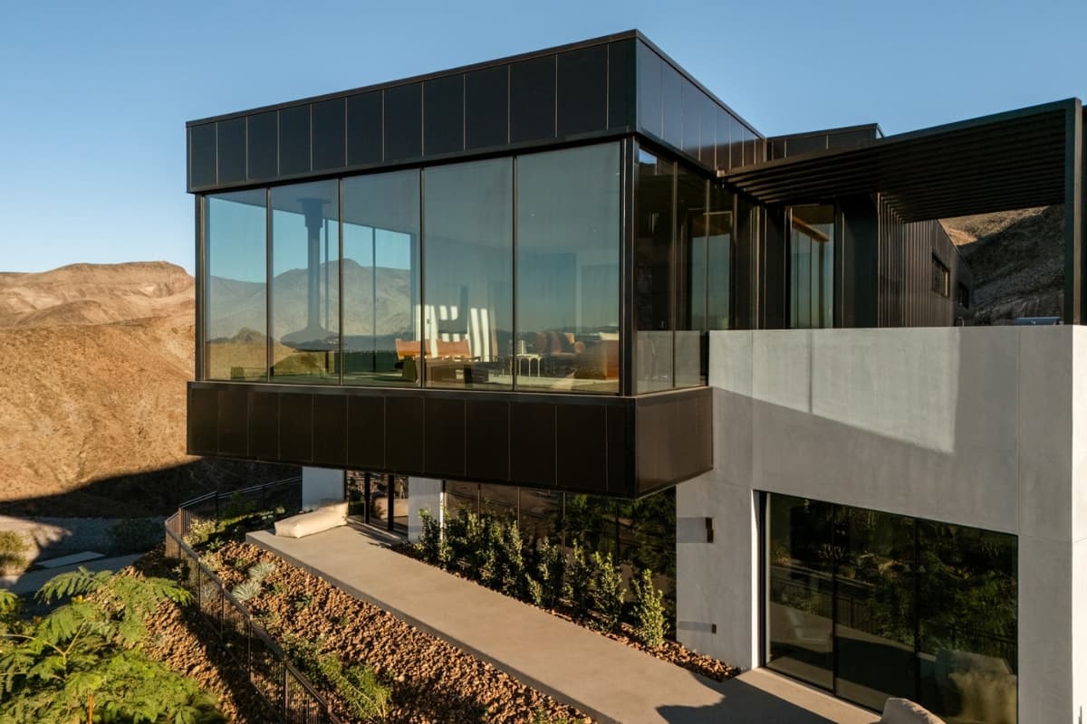 Modern luxury desert home with floor-to-ceiling glass walls and panoramic mountain views.