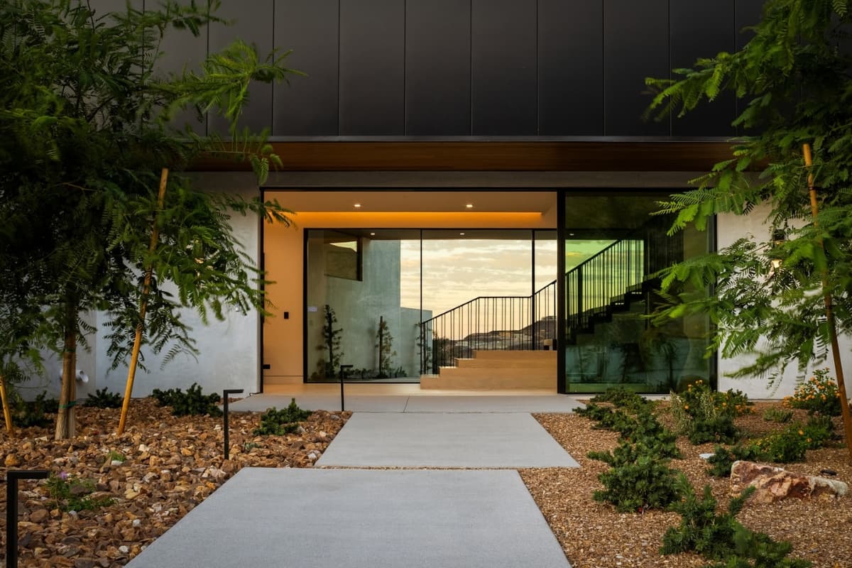 Modern luxury home entrance with floor-to-ceiling glass and landscaped gardens.