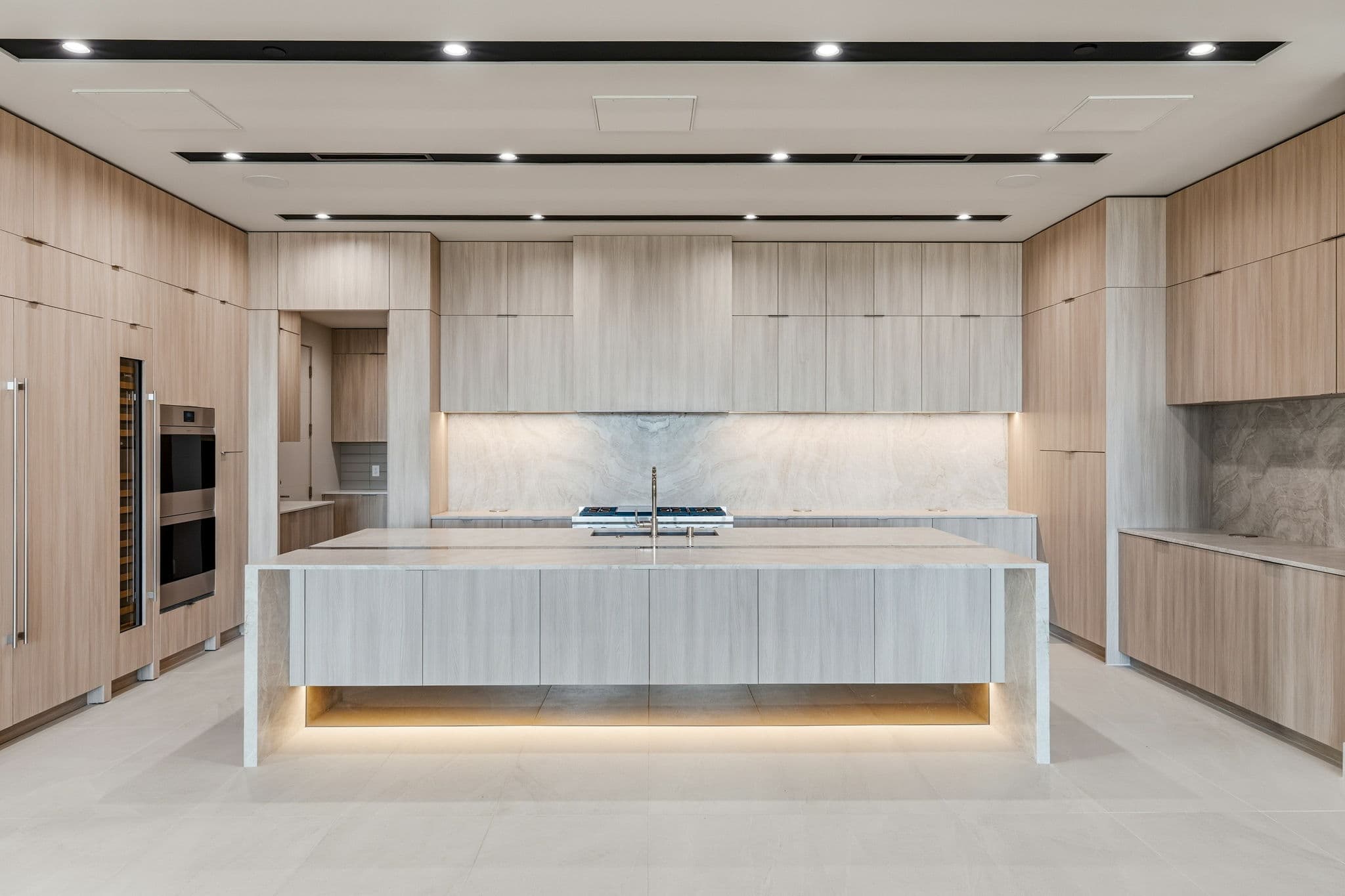 Designer kitchen with a waterfall-edge island, custom wood cabinetry, integrated appliances, and natural stone backsplash