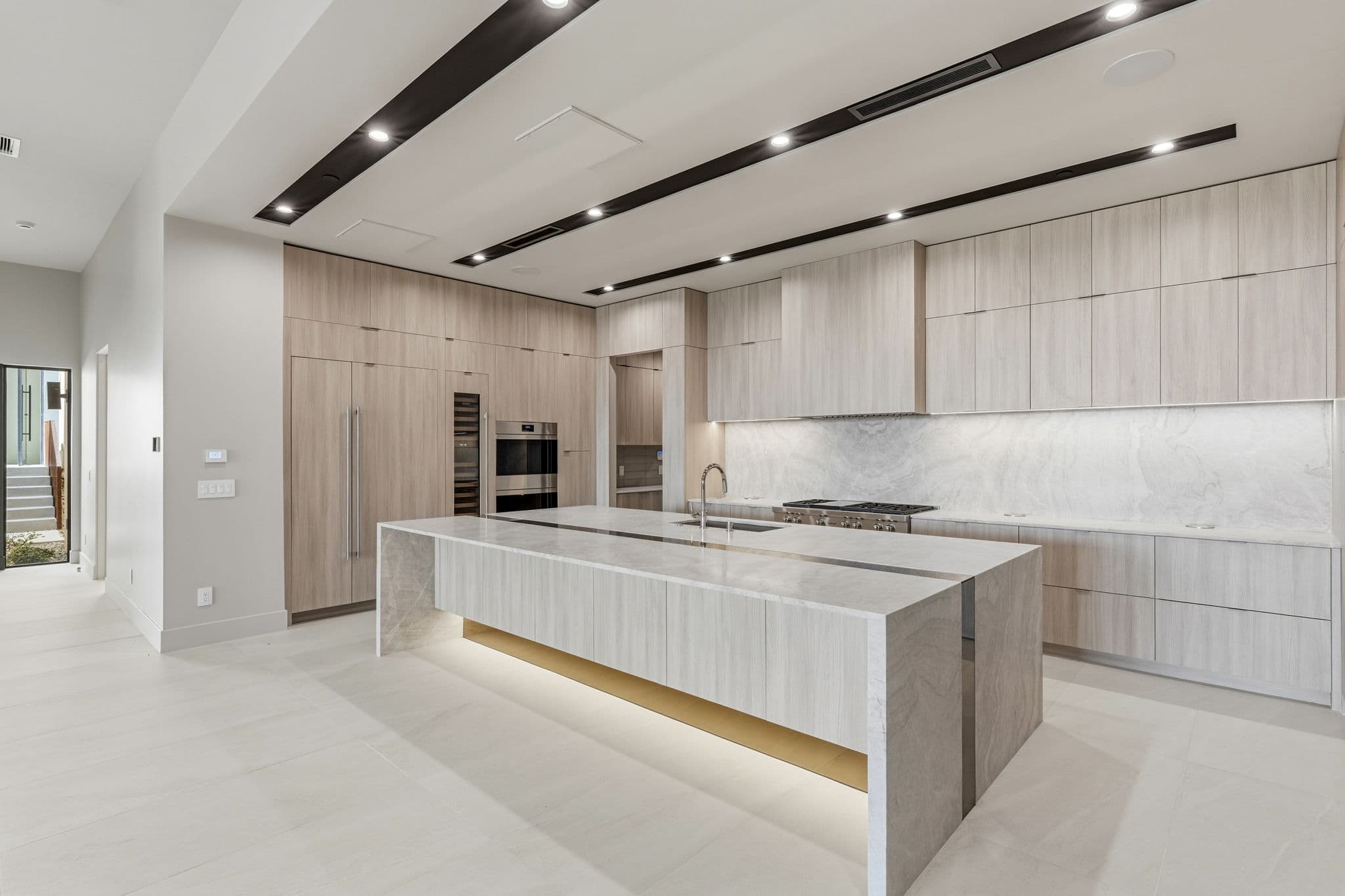 Spacious chef’s kitchen with illuminated waterfall-edge island, custom cabinetry, premium appliances, and elegant stone finishes