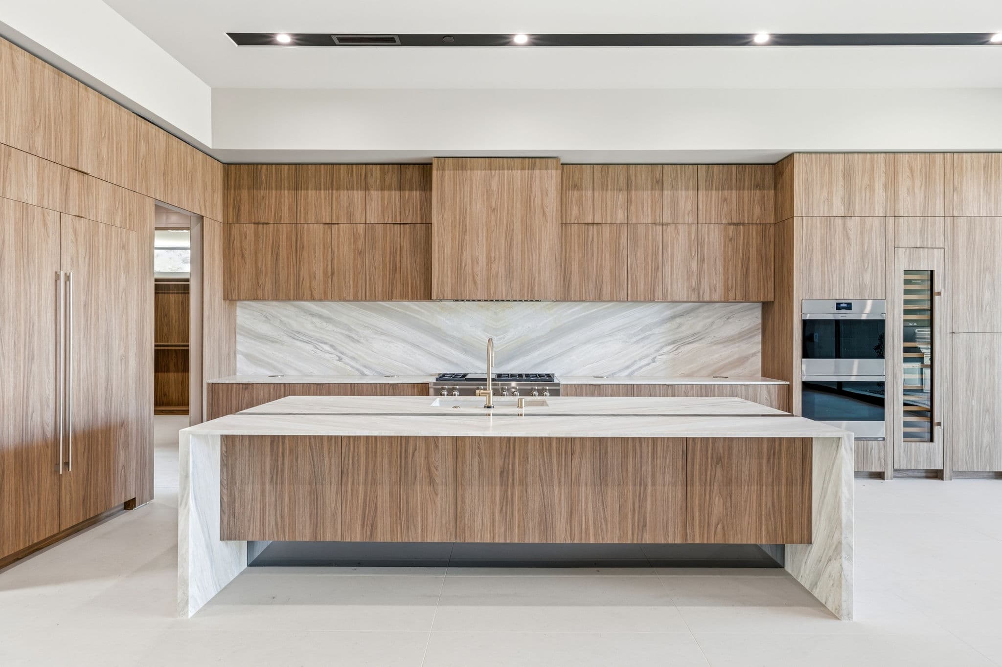 Contemporary chef’s kitchen with waterfall island, custom wood cabinetry, integrated appliances, and marble backsplash