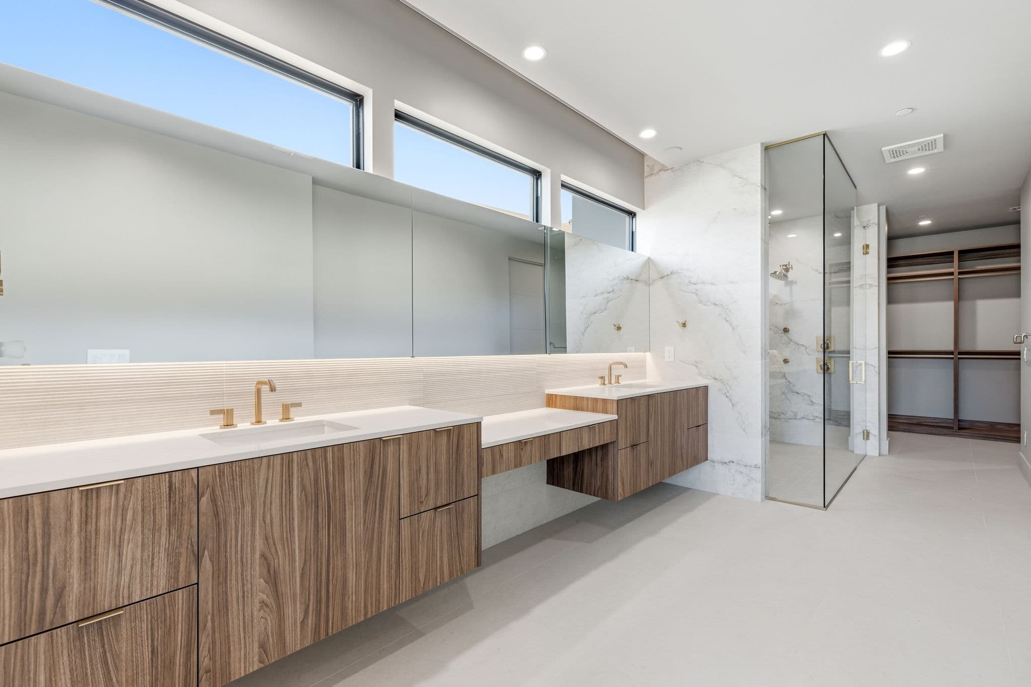 Contemporary bathroom with dual floating vanities, oversized glass shower, marble finishes, and custom walk-in closet access