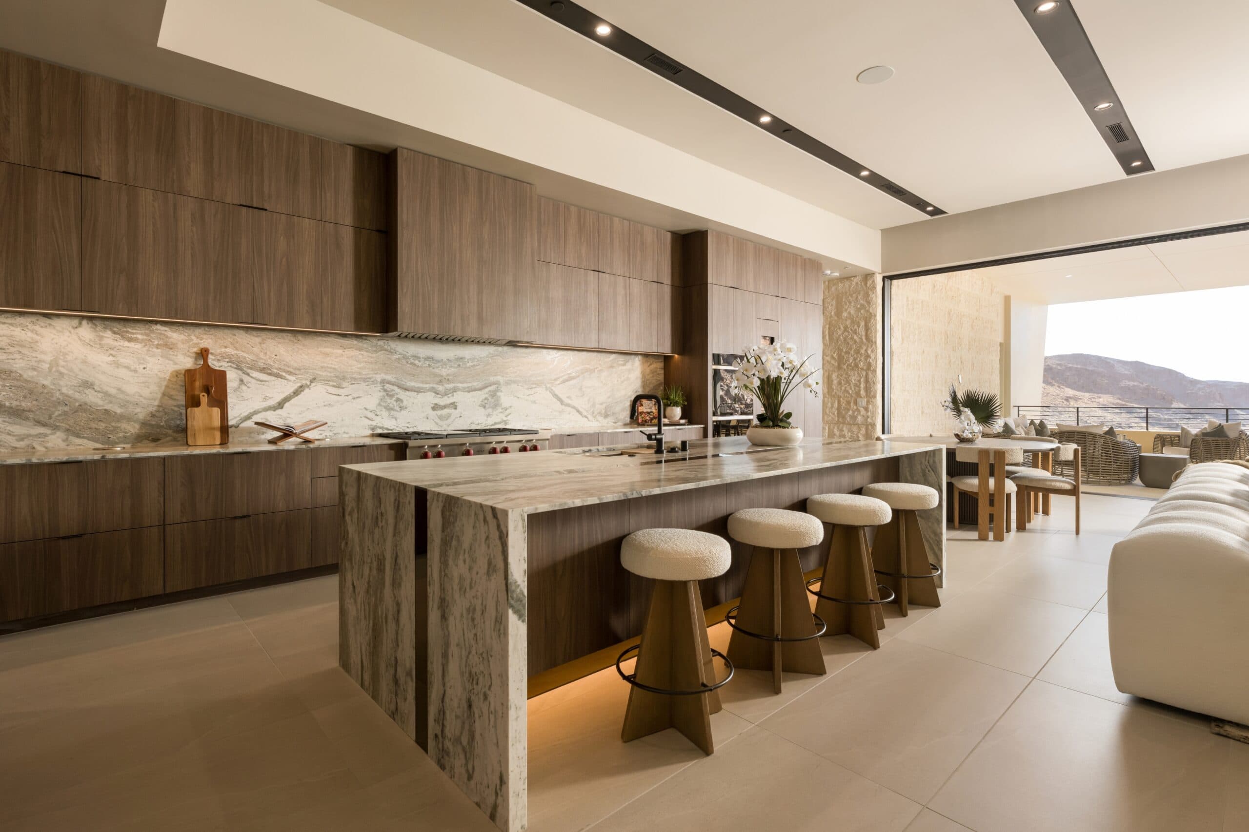 Luxury open-concept kitchen with rich wood cabinetry, marble countertops, a large island, and seamless indoor-outdoor mountain views.