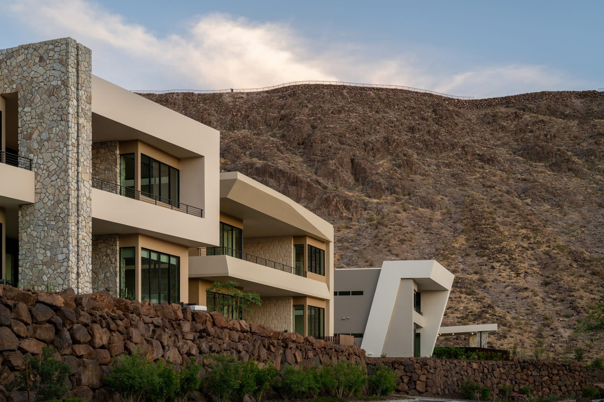 Modern luxury hillside residences with bold geometric architecture, stone accents, expansive windows, and dramatic desert mountain surroundings.