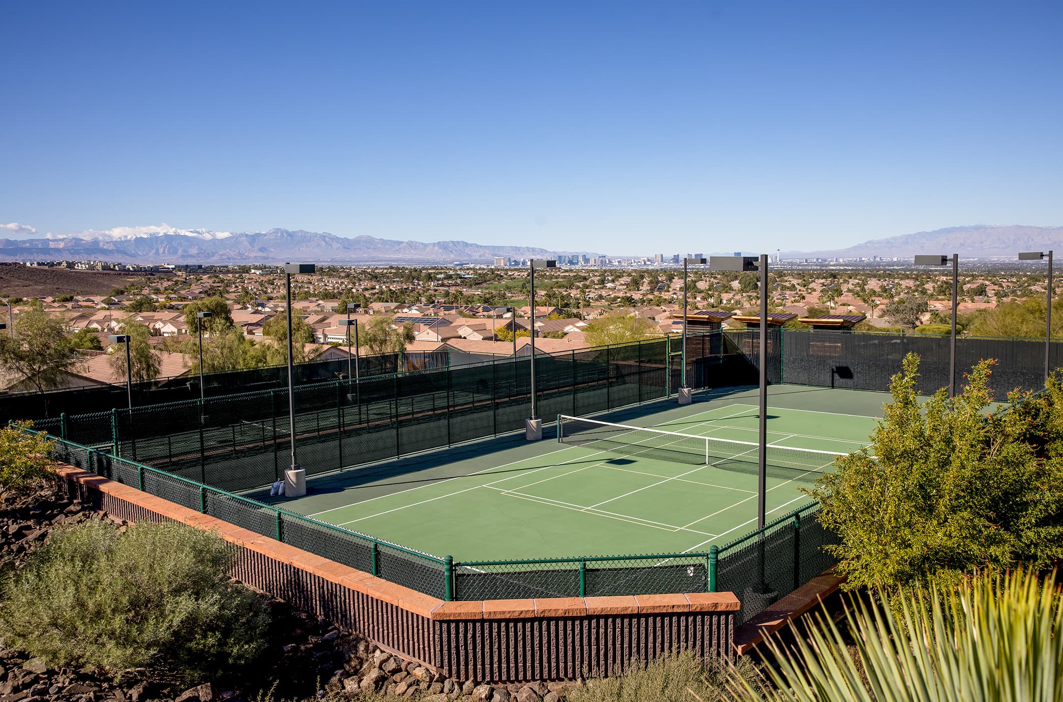 A tennis & pickleball pavilion set above the valley, featuring a full court, perimeter fencing, and sweeping views of the Las Vegas skyline and surrounding mountains.