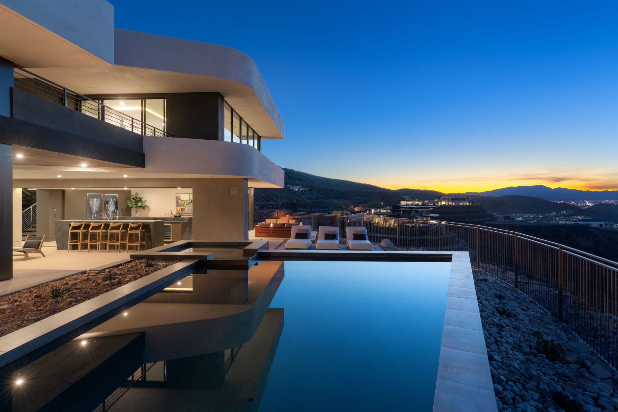 Luxury modern hillside home at dusk featuring an infinity-edge pool, expansive outdoor entertaining spaces, and panoramic mountain and city views under a twilight sky.