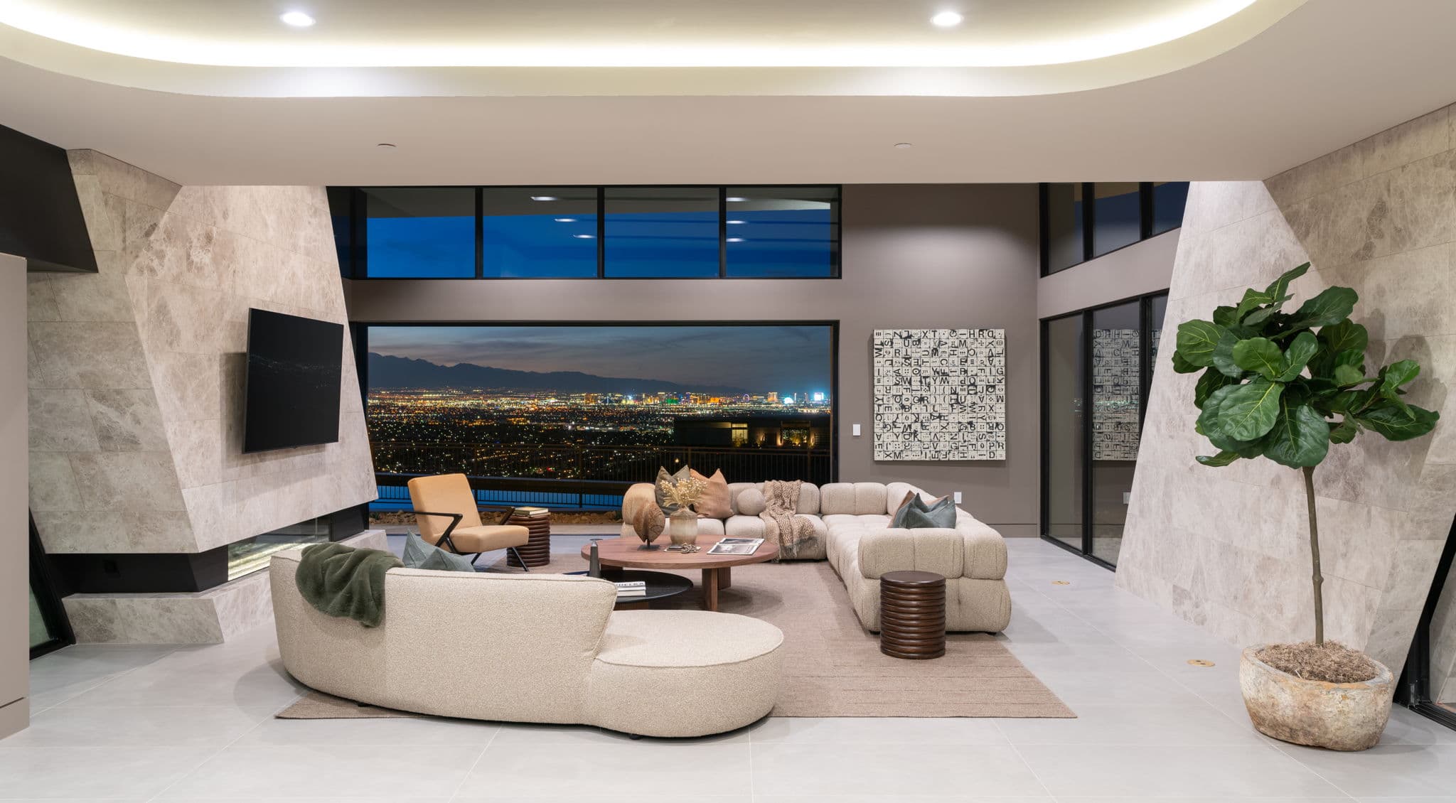 Modern luxury great room with sculptural contemporary furnishings, dramatic stone accent walls, floor-to-ceiling windows, and sweeping nighttime views of the Las Vegas skyline.