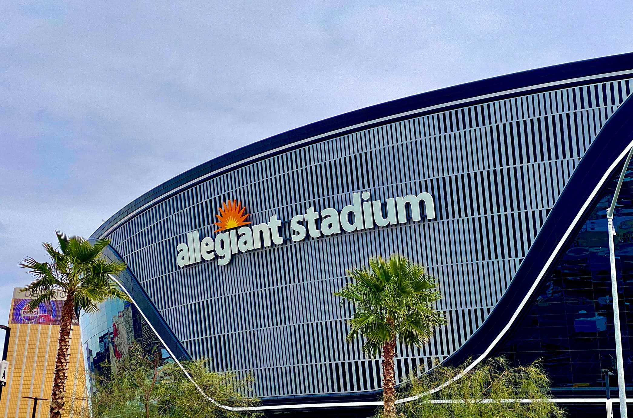 Allegiant Stadium’s striking modern exterior in Las Vegas, featuring its curved architecture, signature facade, and surrounding palm-lined landscape.